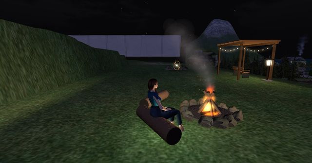 Me on a log seat by the fire pit at night, smoke drifting, the pergola lights behind.
