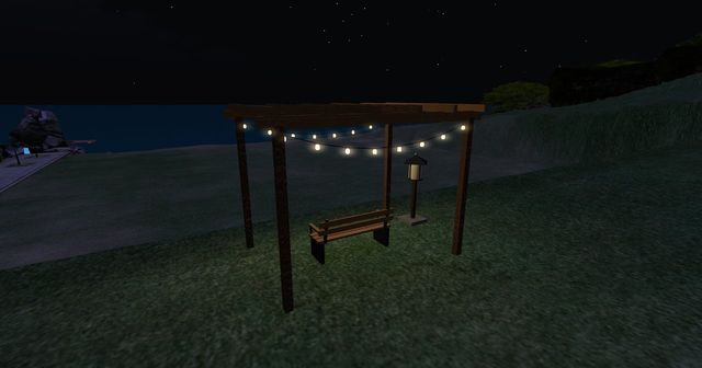 The pergola at night, strings of little lights over the bench, the dark sea beyond.